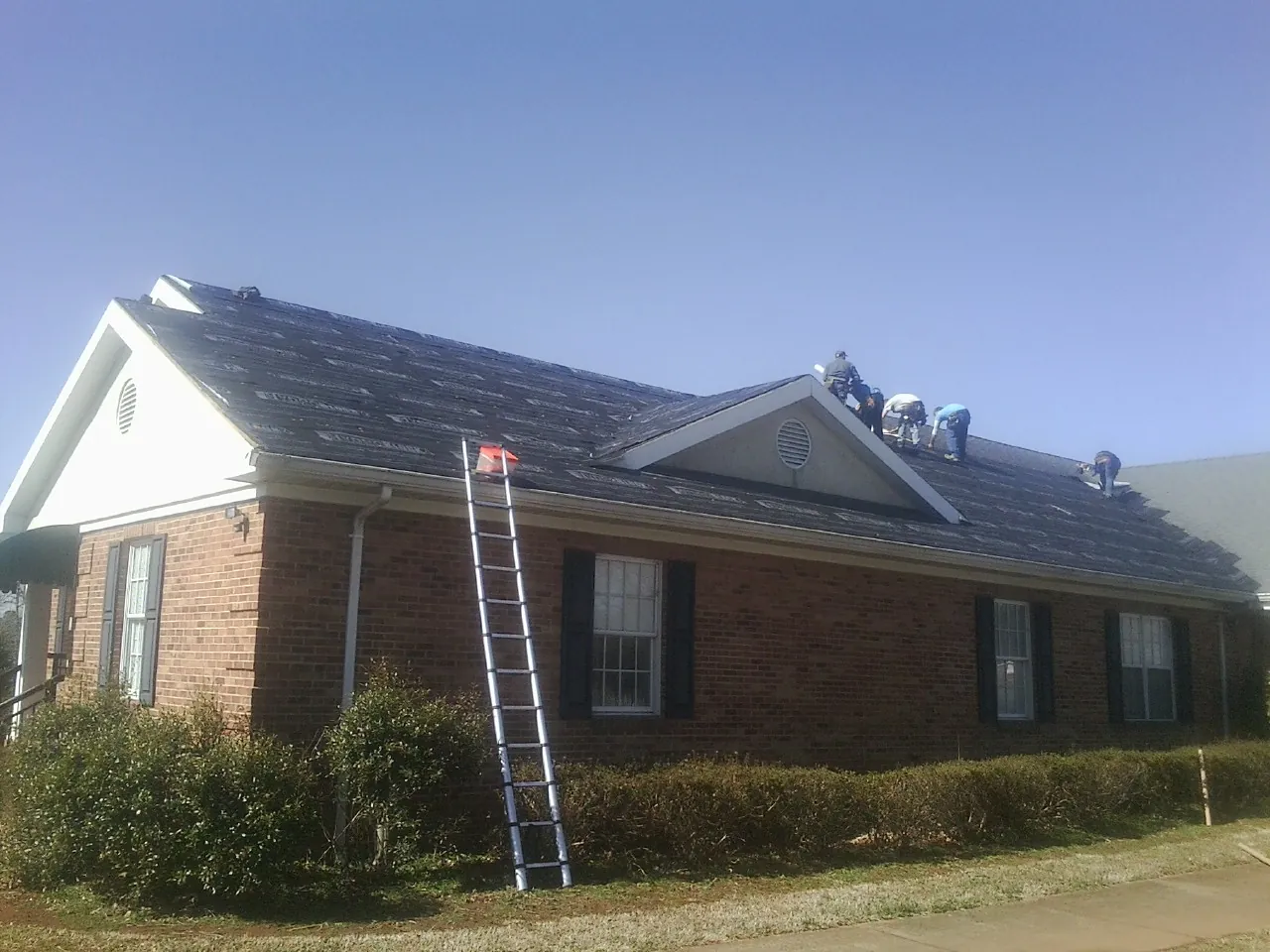 Crew tearing shingles off a brick ranch roof with a ladder set — Emergency Roof Repair work by our crew in Cumberland