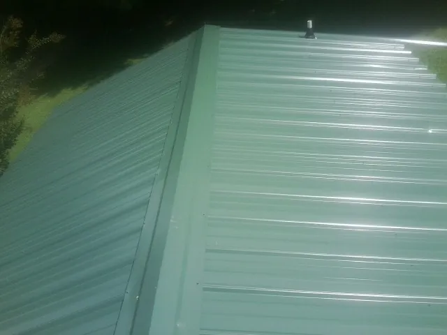 New green metal panels meeting at the ridge of a roof — Flat Roof Repair work by our crew in Cumberland