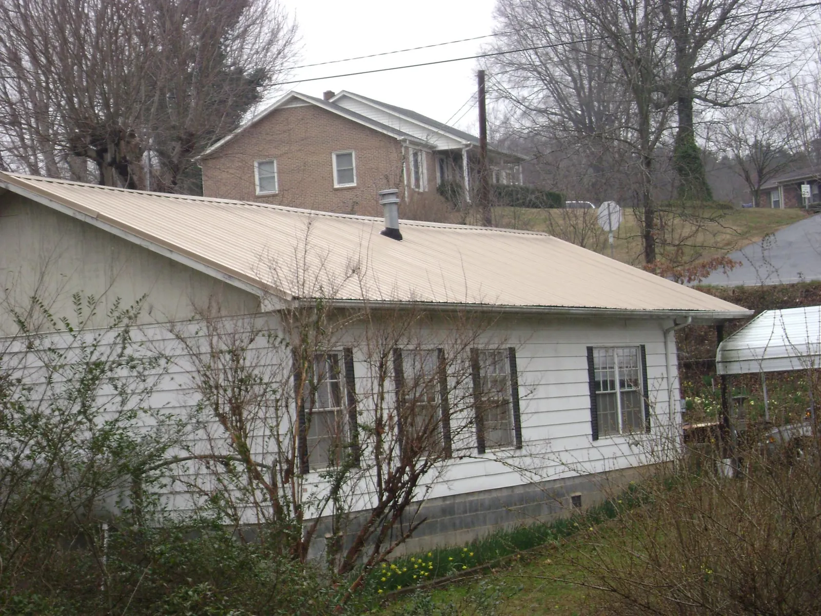 Tan metal roof on a white sided house set into a hillside — Commercial Roofing by Roofing Brothers in Cumberland